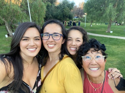 The Grannis girls are all huddled together smiling at the camera while outside in a park. From left to right is Emi, Misa, Kina, and Mama G. The Grannis girls are all huddled together smiling at the camera while outside in a park. From left to right is Emi, Misa, Kina, and Mama G.