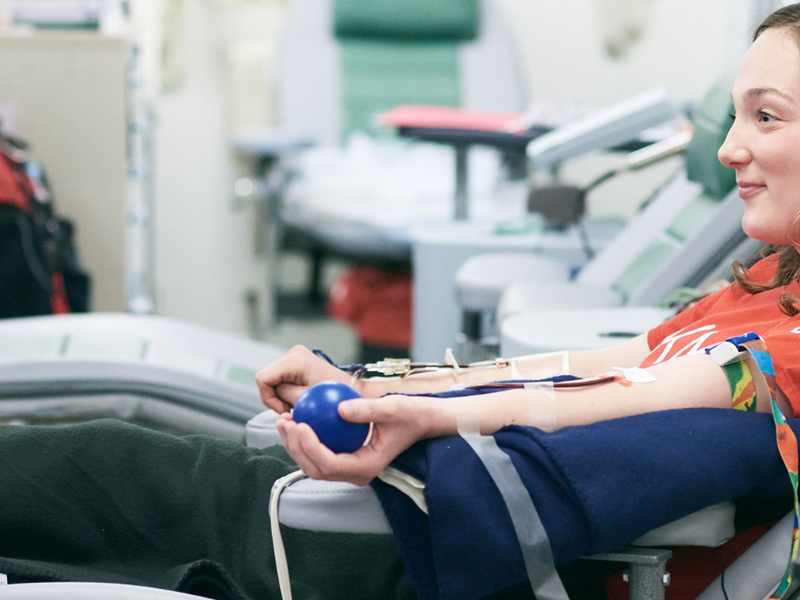 Sideview of a DKMS donor sits in a hospital chair as she donates blood stem cells