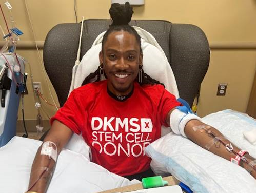 DKMS Blood Stem Cell Donor, Deonte, sitting in a chair donating his stem cells while smiling wearing a DKMS donor shirt. 