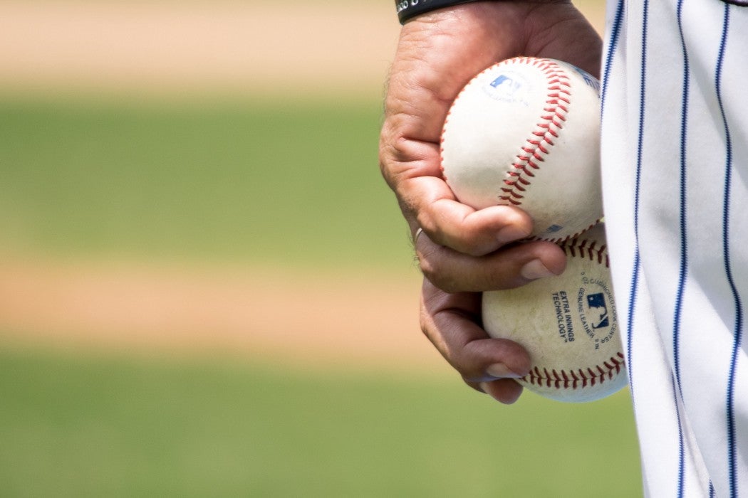 Close-up of a baseball player's hand holding two baseballs, wearing a striped jersey