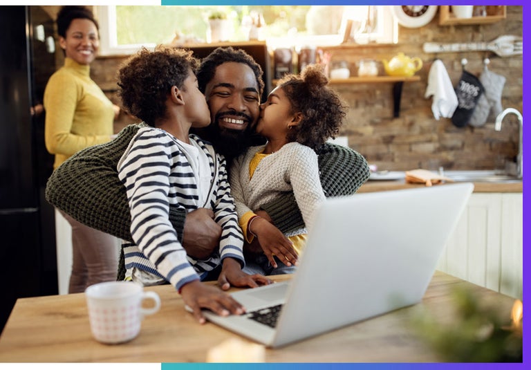 A dad squeezes his two daughters while working from home.
