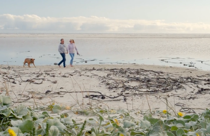 Jeremy Swartz walking along a beach with his wife and dog