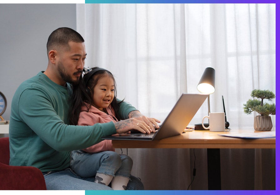 An Asian dad works from home with his daughter on his lap.