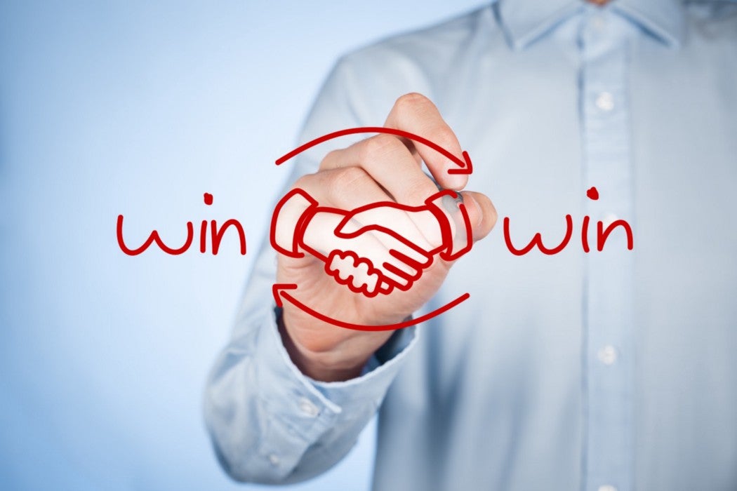 A person in a light blue shirt drawing a handshake symbol and the phrase 'win-win' on a transparent screen
