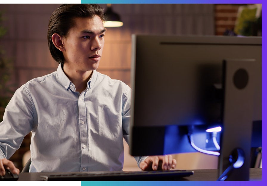 An Asian man sits at his computer doing remote work. 