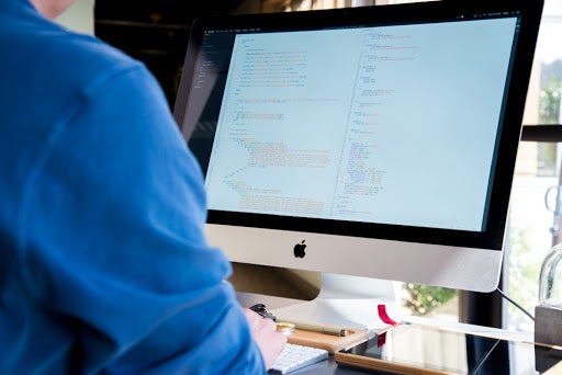 Rear view of a person coding on an iMac computer, displaying lines of code on the screen