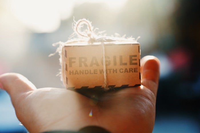 lose-up of a small cardboard box labeled 'FRAGILE: HANDLE WITH CARE' being held carefully in a person's hand