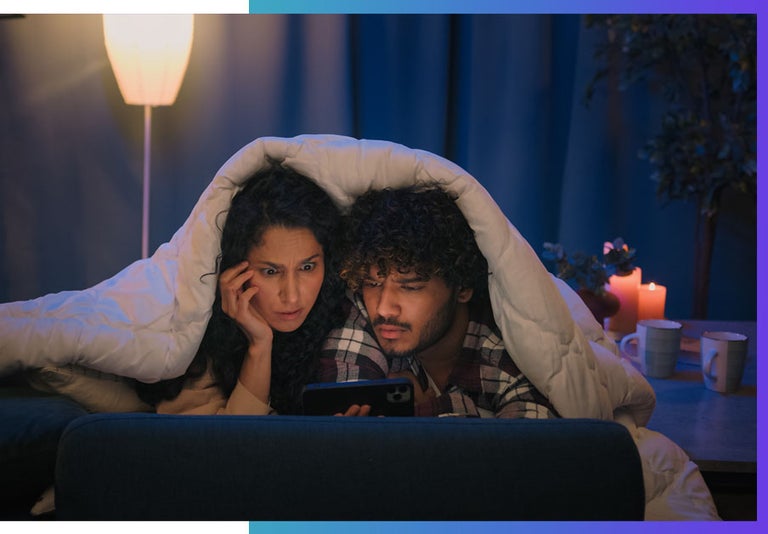 Screens and blue light keep you awake at night. A couple watch their screens before bed.