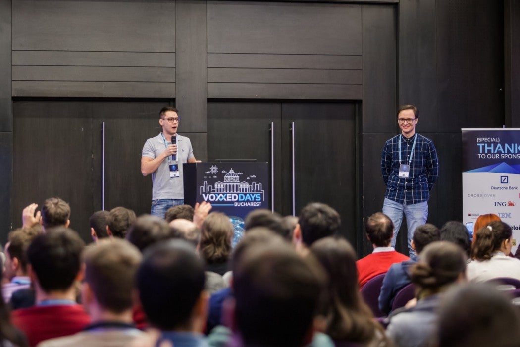 Two men presenting in front of a large audience at a technology conference