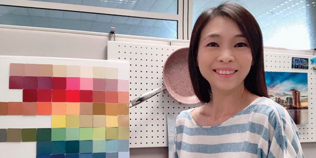 Karen Tyng Cowell, PPG's APAC marketing manager, smiling with color swatches from PPG's kitchenware coatings and a pink frying pan.