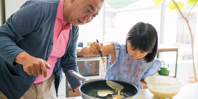 Padre e figlia in cucina preparano frittelle in una padella con rivestimento antiaderente a basso attrito.