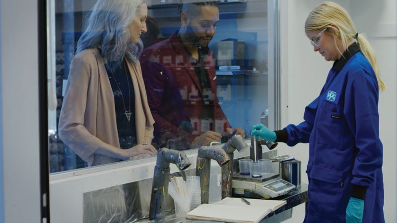 Color technician mixing coating colors in PPG's color studio with clients watching behind a protective, clear screen.