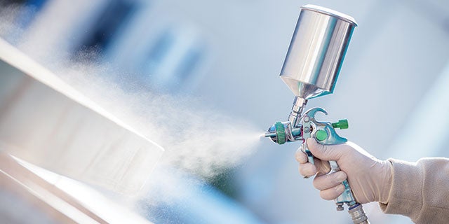 PPG paint applicator spraying liquid coating onto metal infrastructure using a spray gun.