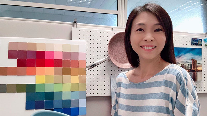 Karen Tyng Cowell, PPG's APAC marketing manager, smiling with color swatches from PPG's kitchenware coatings and a pink frying pan.