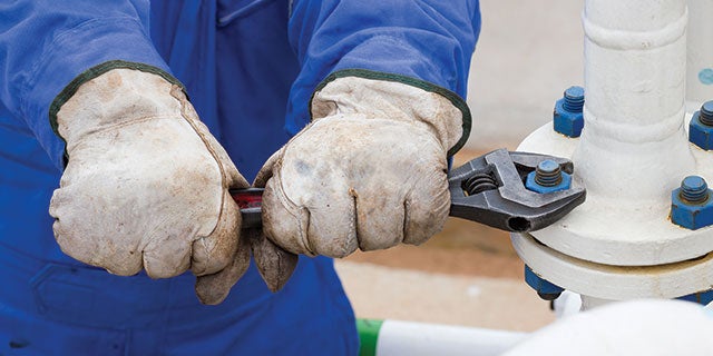 Primer plano de las manos de un trabajador utilizando una llave inglesa para apretar un tornillo en una tubería de metal blanco protegida con revestimientos para tornillería de PPG.