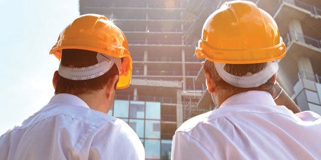Two workers wearing hard hats examining building