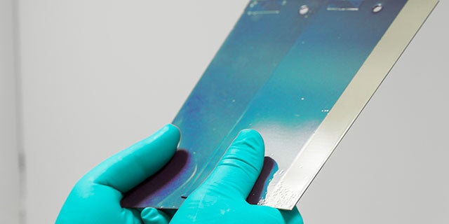 Close-up of two color samples on a metal surface with gloved hands holding them.