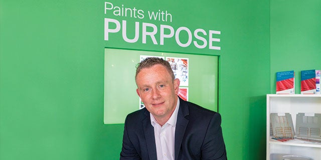 Mark Poland, PPG's technical manager, smiling in front of green background displaying paints with purpose.