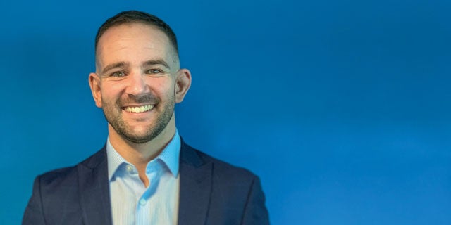 David Linford, PPG's global key account manager and strategic segment manager, smiling wearing a blue suit in front of a blue background.