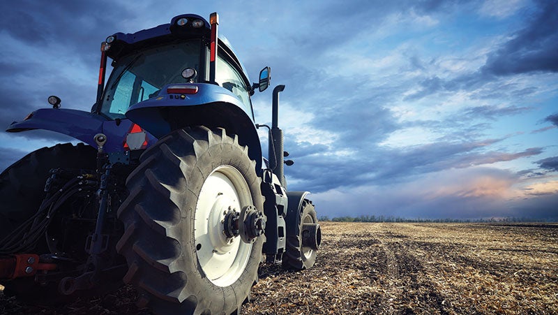 Blue tractor, protected by PPG's coatings for heavy-duty agricultural equipment, in a field with a cloudy blue sky.