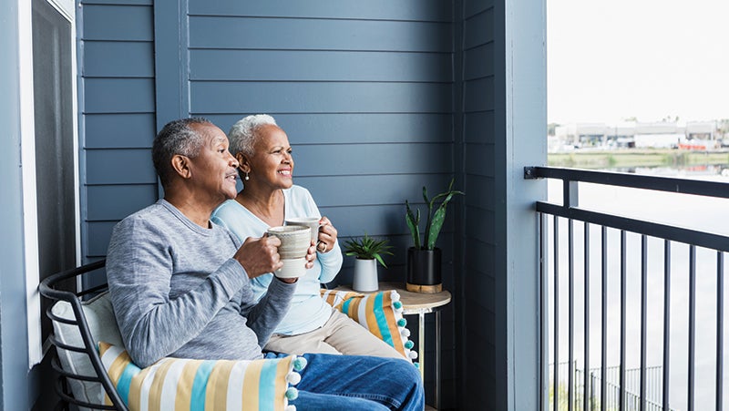 A couple sat on a balcony looking at the view and drinking from a mug each.