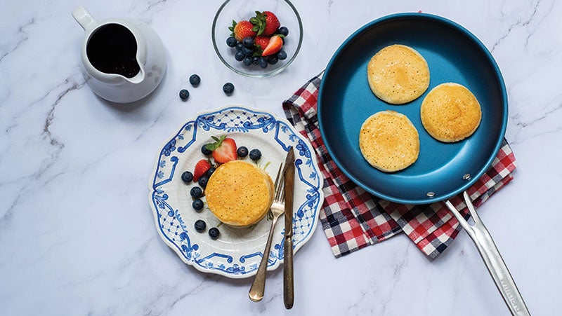 A blue frying pan, protected by PPG Eclipse nonstick coating, containing pancakes with berries on the side in a bowl