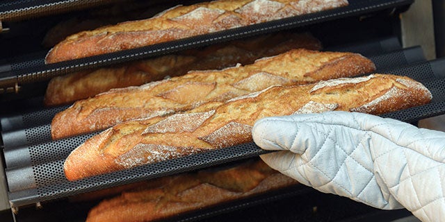 Un panadero saca baguettes de un horno industrial con guantes de cocina.