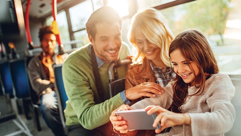 Mother and father sat on a bus with daughter all looking at a mobile phone together which is protected by PPG's electronics coatings.