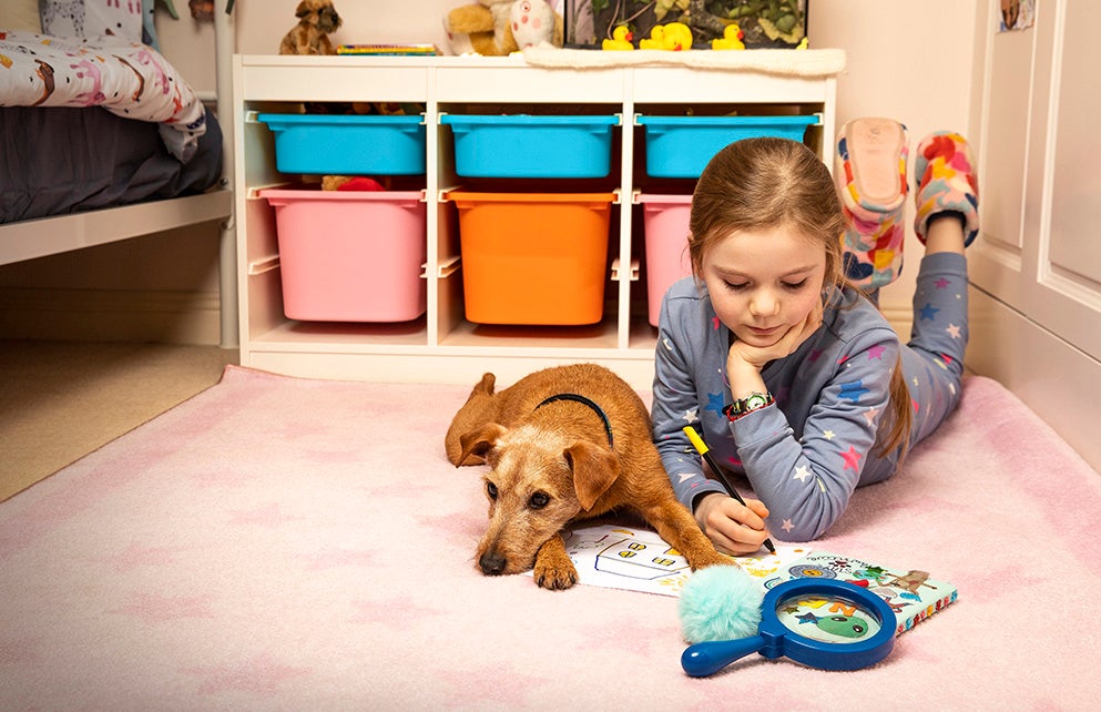 Girl drawing with dog in bedroom.