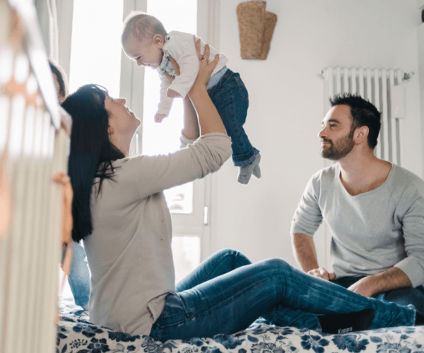 woman holding laughing baby in the air with man watching