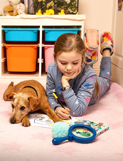Girl writing in book with dog beside her.