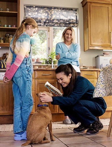 Service engineer playing with dog in kitchen while mother and daughter look on.