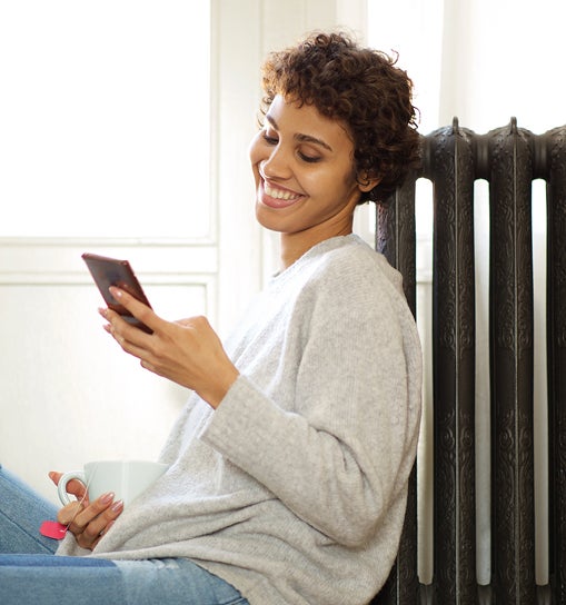 Woman leaning against a radiator looking at her smartphone