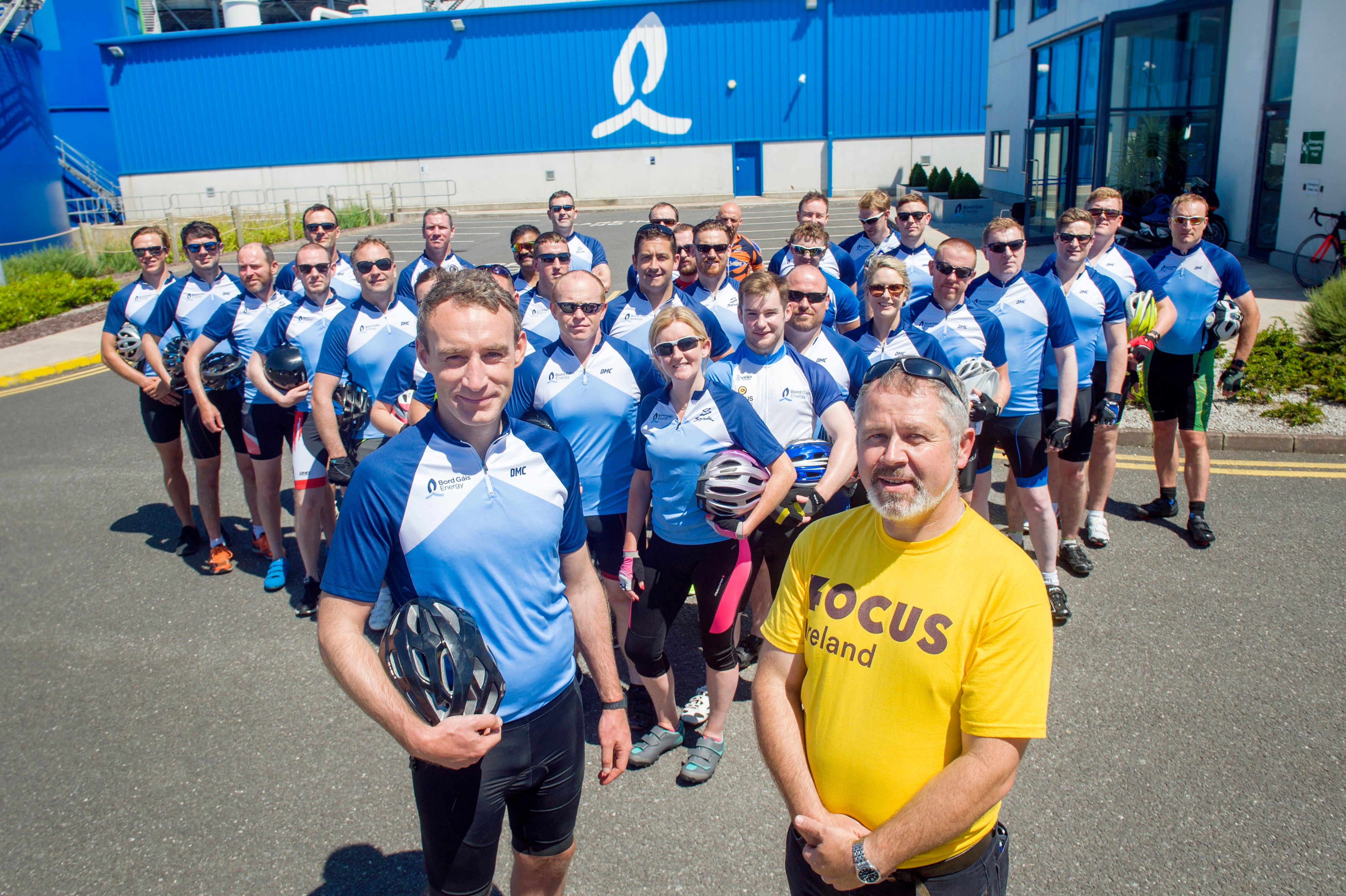 Cyclists in blue holding helmets and man wearing yellow focus ireland t-shirt
