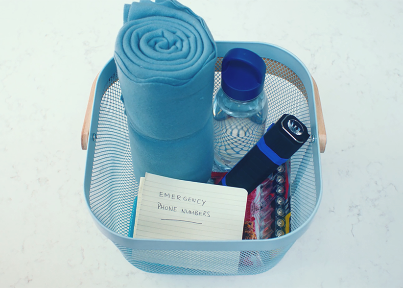 A basket containing emergency provisions including a blanket, batteries, a torch and emergency phone numbers.