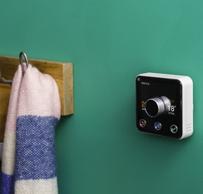 Hive thermostat on a green wall beside a scarf on a coat hook