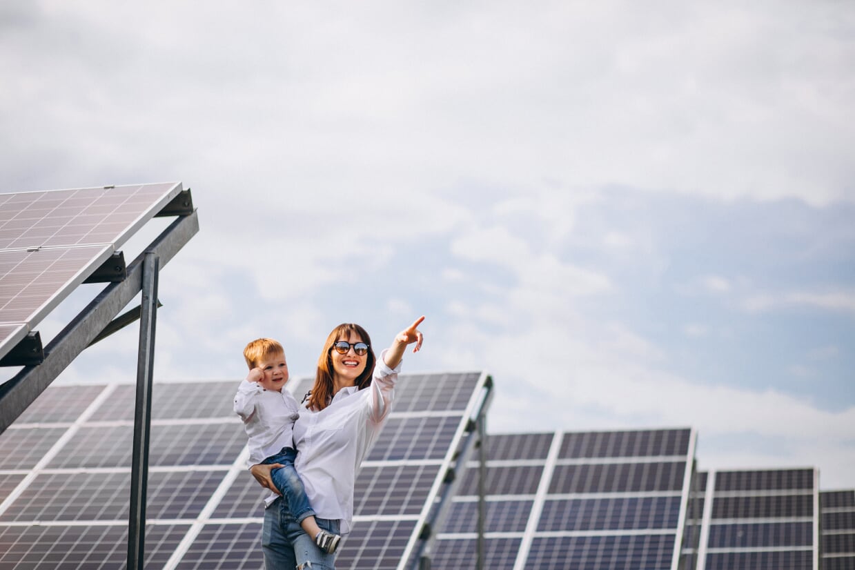 Mother holding infant son beside solar panels.
