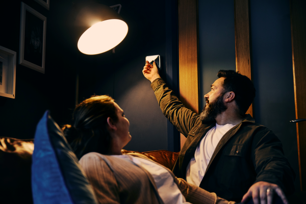 Couple of on the sofa with man adjusting smart thermostat