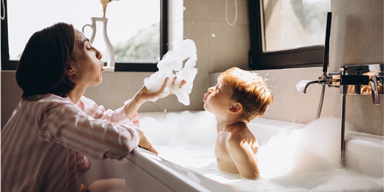 Woman with child in bath blowing bubbles