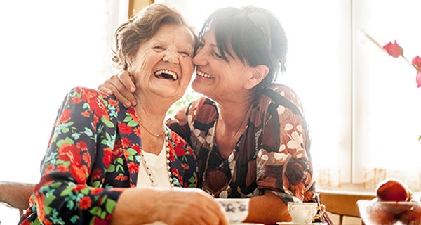 Elderly woman laughing with daughter while having tea