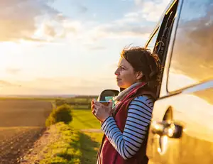 Frau neben Auto auf einem Feld mit Kaffee in der Hand