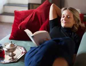 Frau liegt auf der Couch und liest in einem Buch.