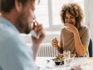 Frau und Mann sitzen beim Essen am Tisch und lachen.