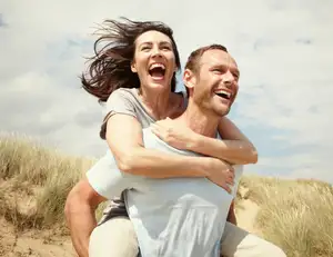 Mann trägt Frau auf dem Rücken beide lachen.