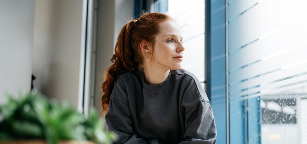 Frau schaut nachdenklich aus dem Fenster.