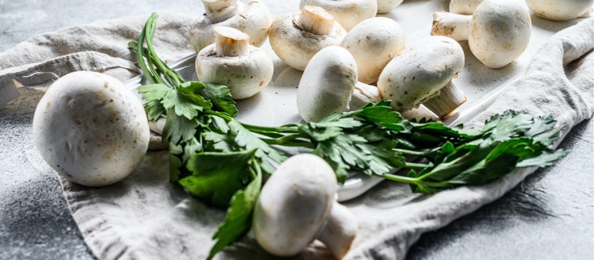 Weiße Champignons und ein Stück Käse auf einem Tisch.