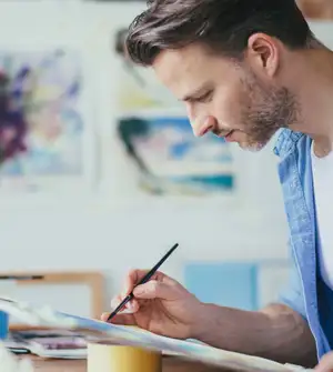 Ein Mann malt mit einen schmalen Pinsel in der Hand.