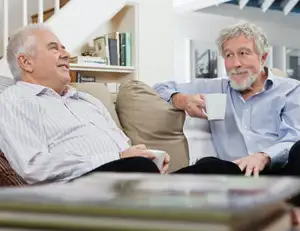 Zwei ältere Männer sitzen auf dem Sofa und trinken Kaffee.