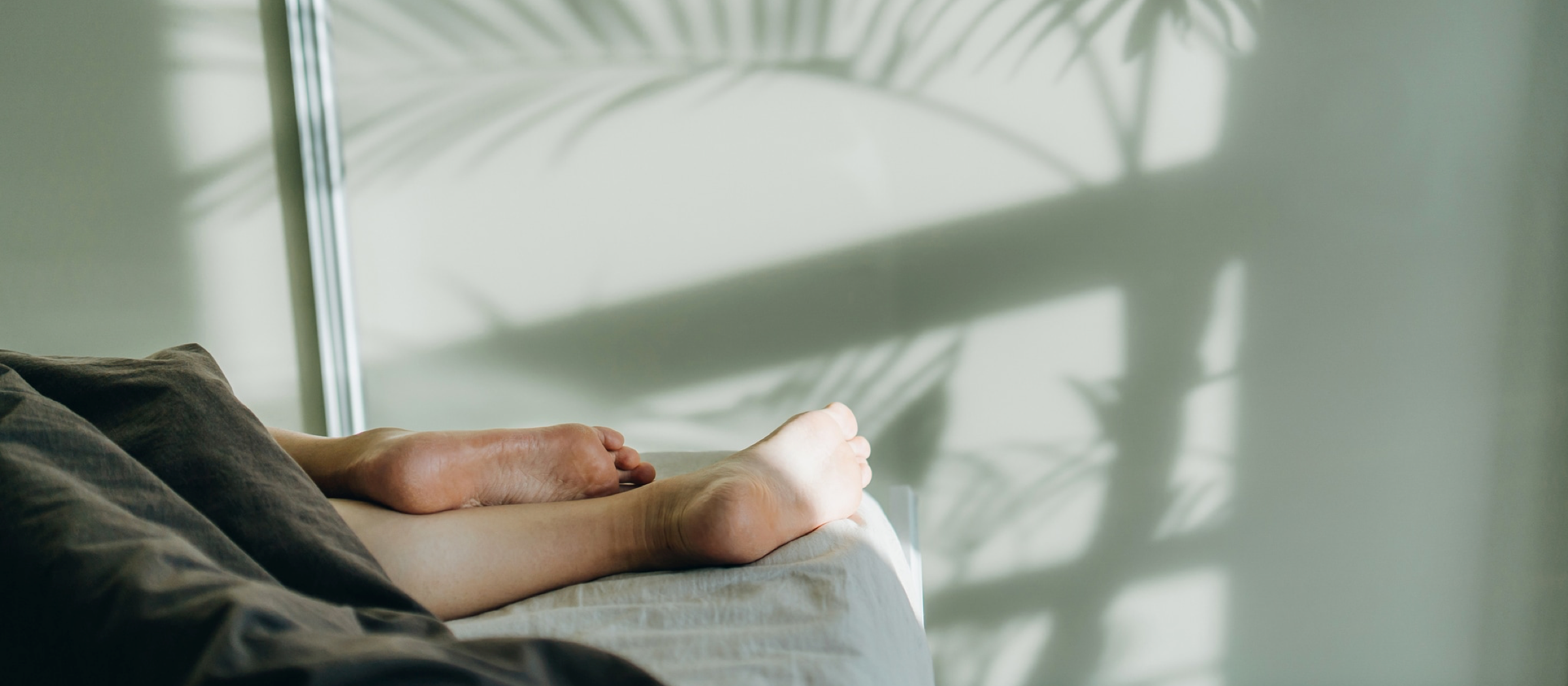 Frau liegt im Bett und schläft und lässt die Füße raushängen.