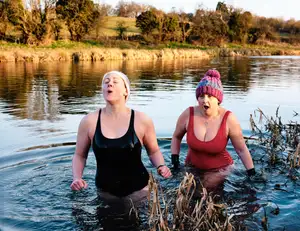 Zwei Frauen in Badeanzug mit Mütze stehen in einem See.